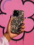 Phone case with black lace floral design, soft pink satin bows, and small pearl accents on a pale nude background; fits iPhone, Samsung, and Pixel models